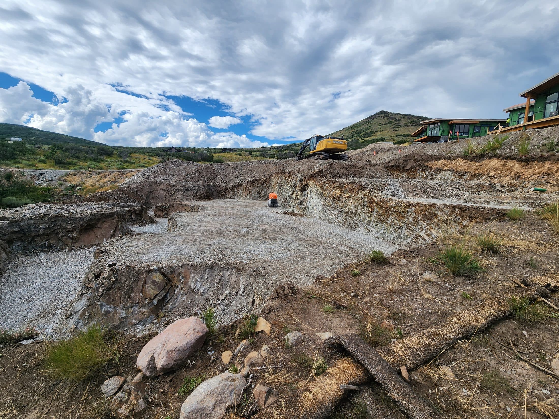 Excavator above a graded site in a mountain neighborhood.